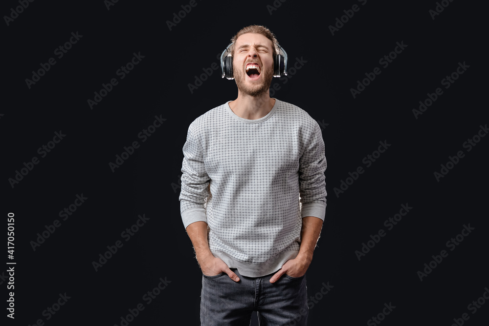 Emotional young man listening to music on dark background