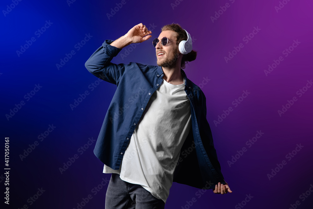 Handsome young man listening to music on dark background