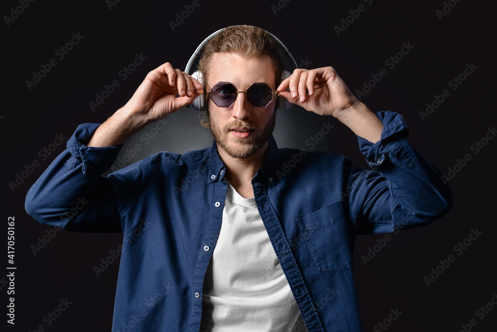 Handsome young man listening to music on dark background