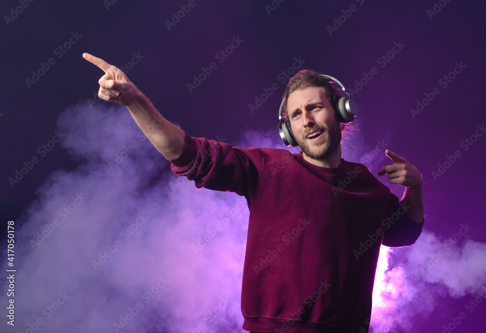 Emotional young man listening to music on dark color background