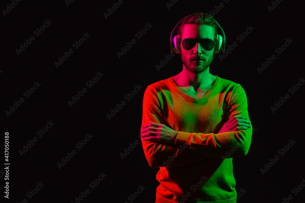 Handsome young man listening to music on dark background