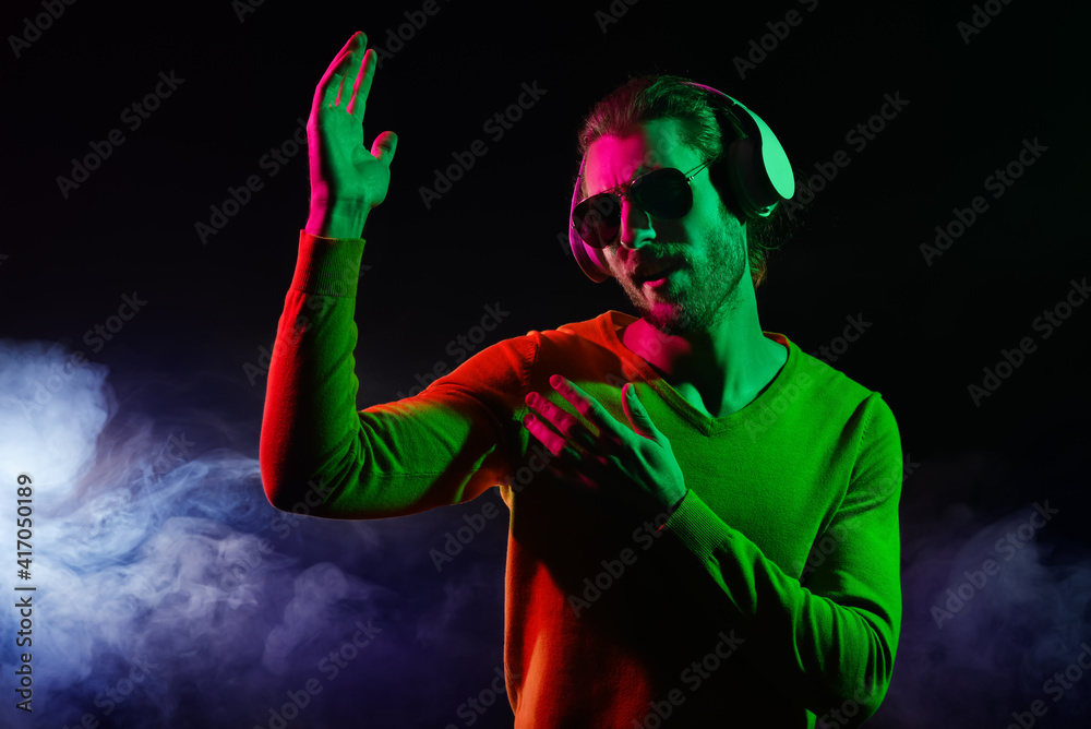 Handsome young man listening to music on dark background