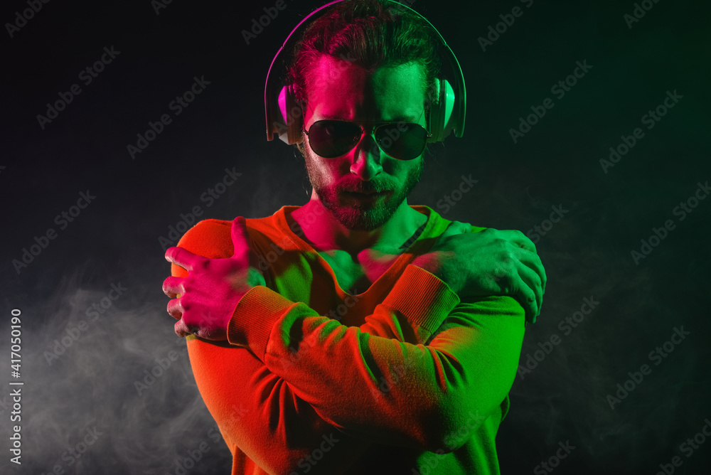 Handsome young man listening to music on dark background