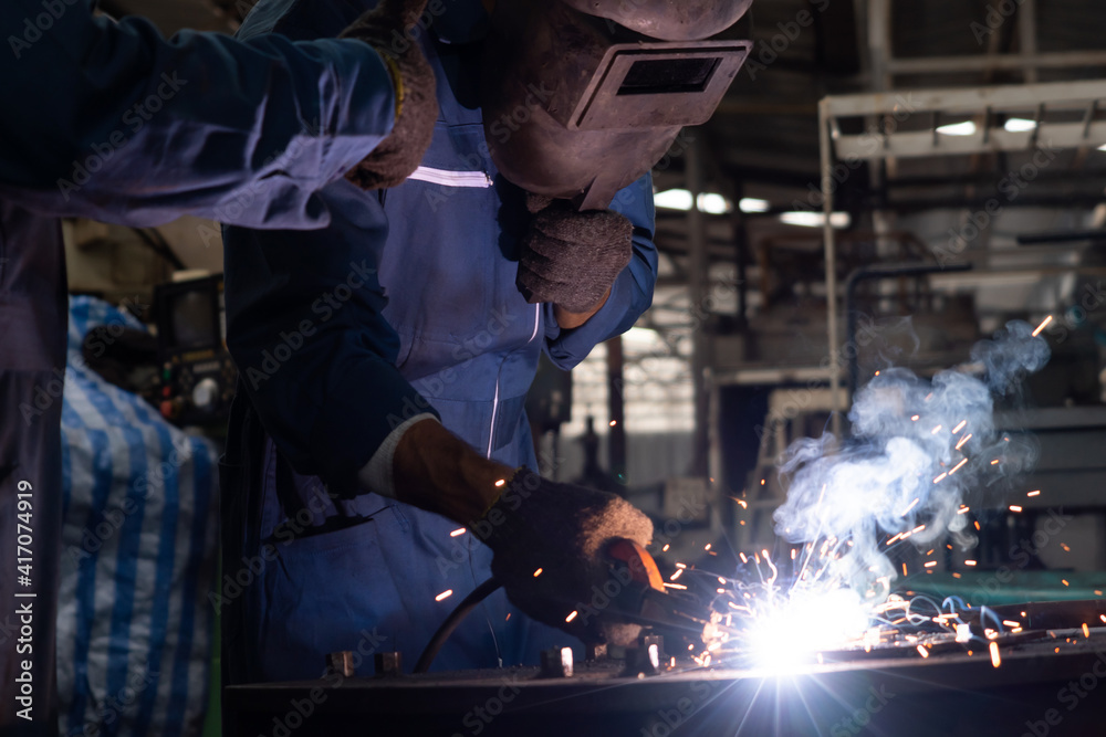 Skillful metal worker working with arc welding machine in factory while wearing safety equipment. Me