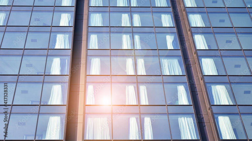 Blue curtain wall made of toned glass and steel constructions under blue sky. A fragment of a buildi