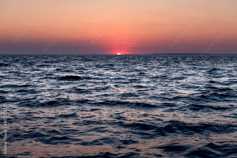 Sunset in the ocean with large sun dusk soft waves and red cloudy sky. Sea sunrise background. Lands