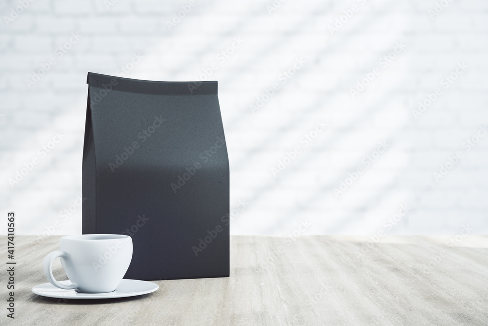 Blank black coffee package with a copyspace and white cup on wooden table. Mockup