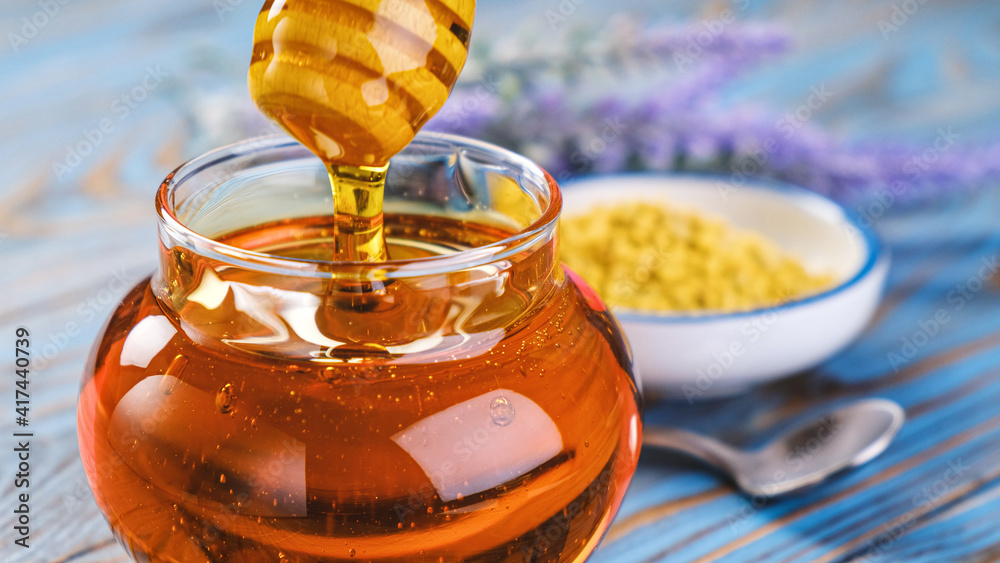 Honey in glass jar with honey dipper over wooden background