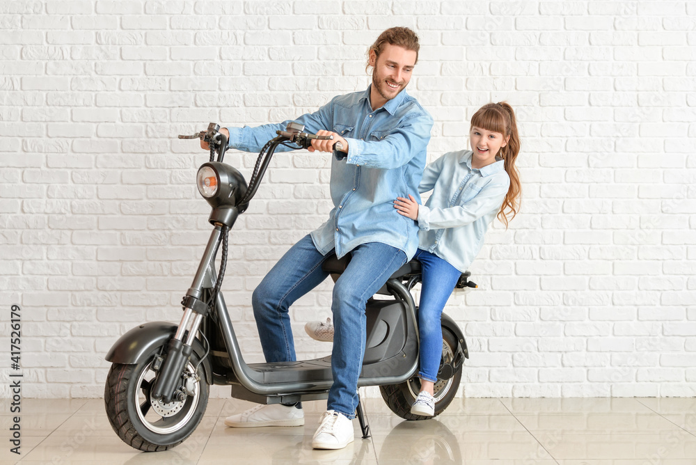 Happy daughter and father with electric scooter near white brick wall