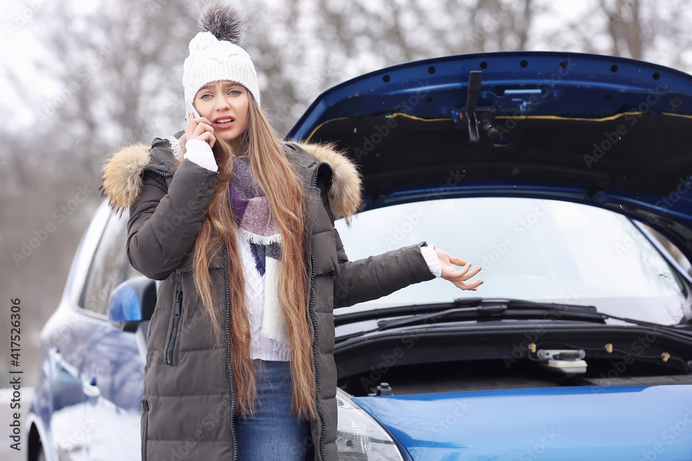 Stressed young woman talking by phone near broken car outdoors