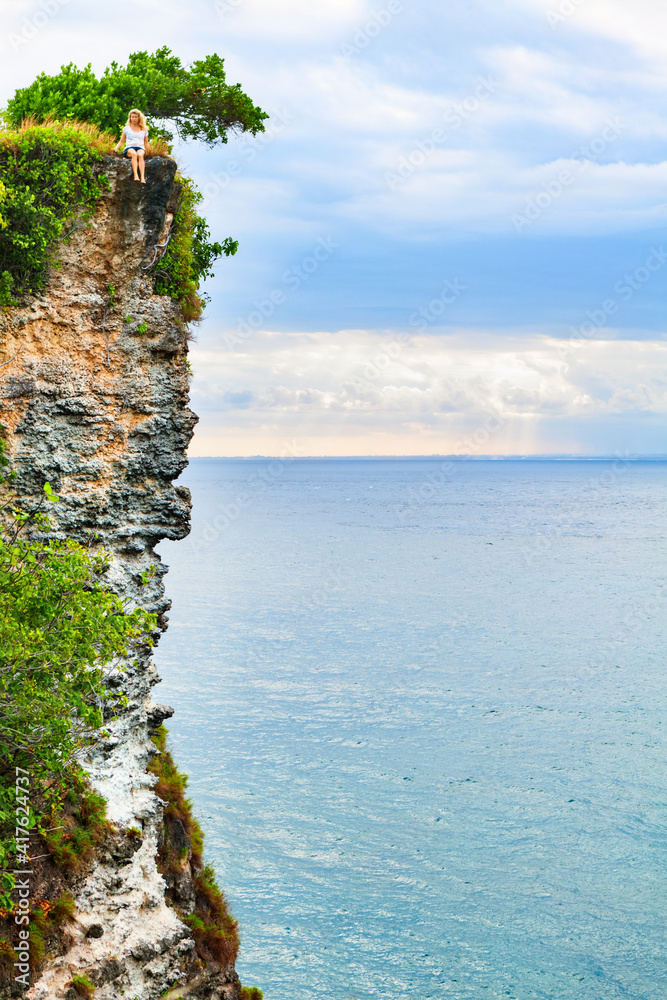 Happy girl have fun on summer beach holiday. Young woman relax at rock cliff above sea. Looking at b