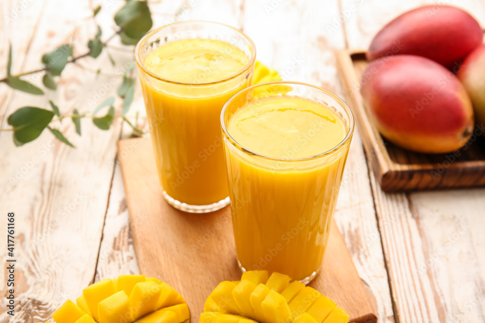 Glasses of tasty mango smoothie on light wooden background