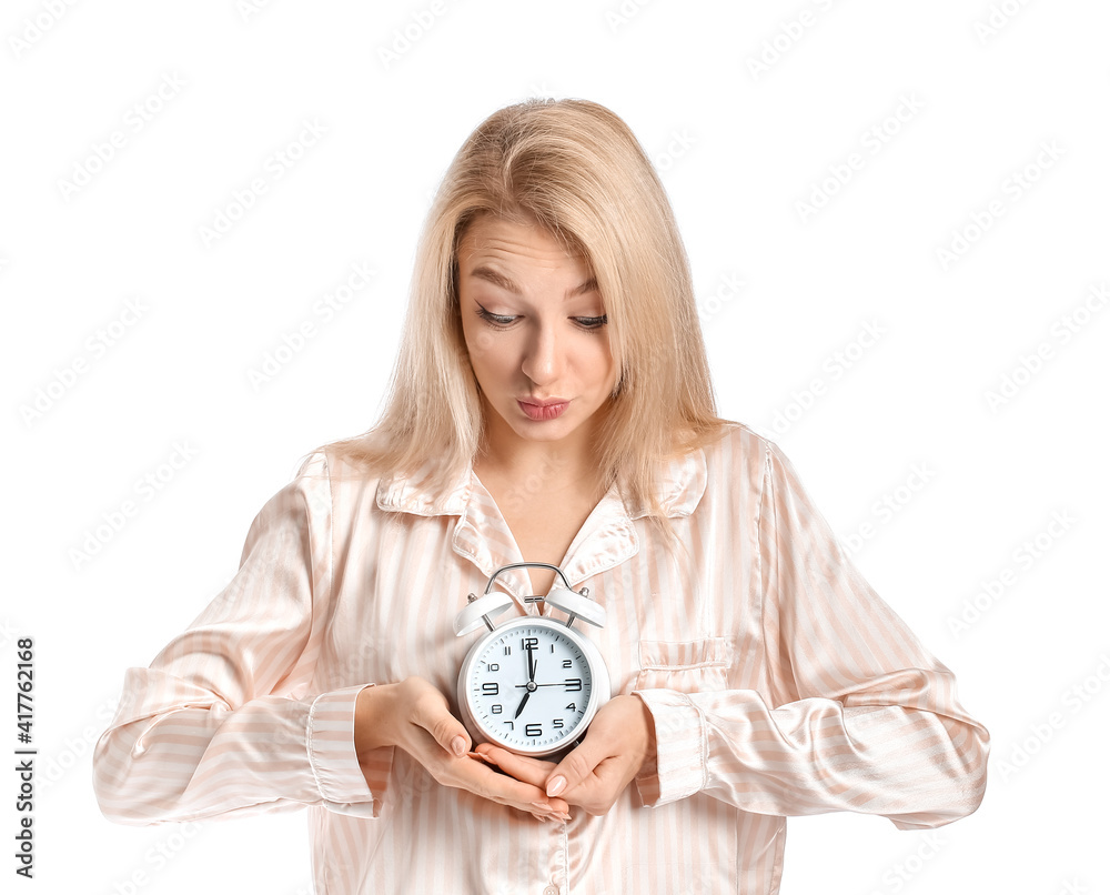 Stressed young woman in pajamas and with alarm clock on white background