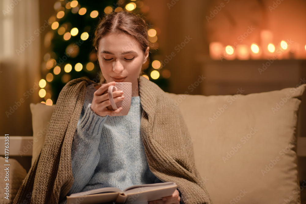 美丽的年轻女子在圣诞前夜喝热巧克力，在家看书