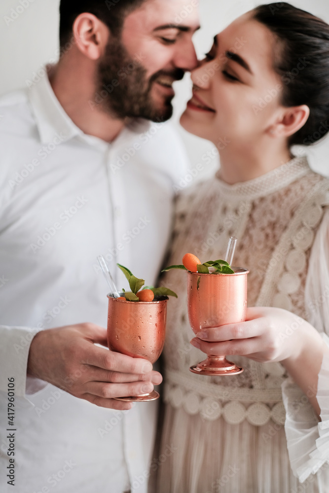 Smiling romantic loving caucasian couple celebrating holiday with ice cocktail with citrus in brass 