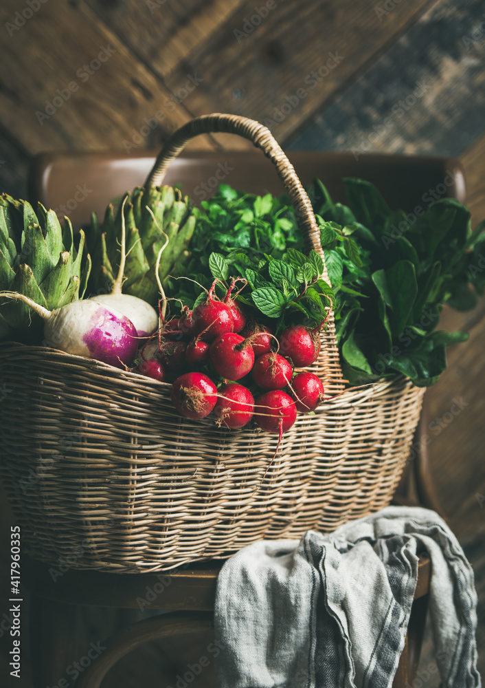 Basket of fresh organic garden vegetables and greens on chair, rustic wooden wall at background