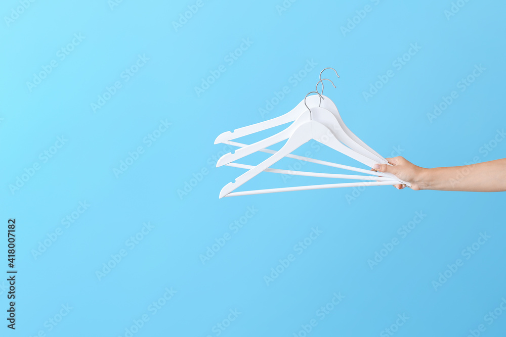 Woman holding clothes hangers on color background