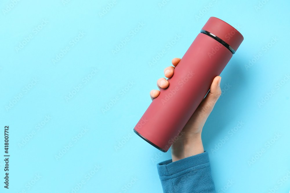 Female hand with modern thermos on color background