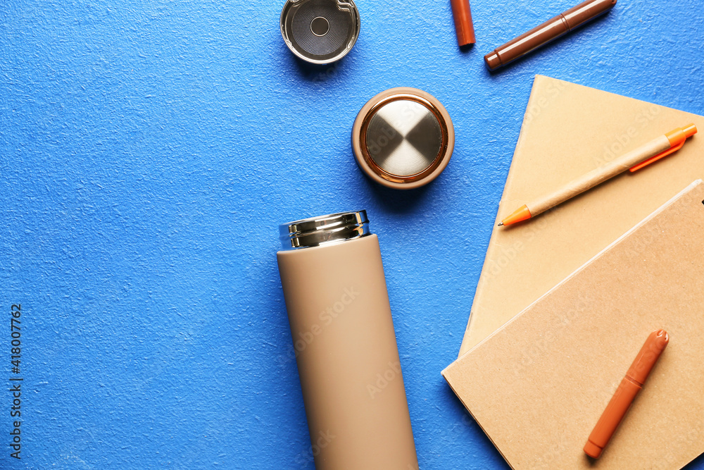 Modern thermos and stationery on color background