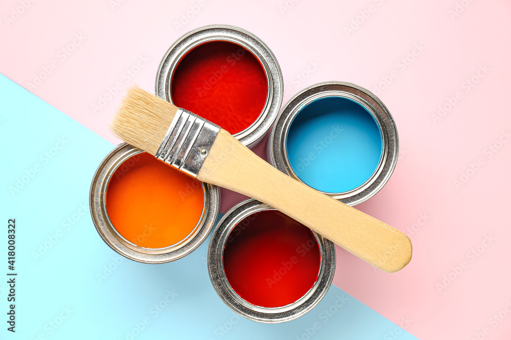 Cans of paints and brush on color background