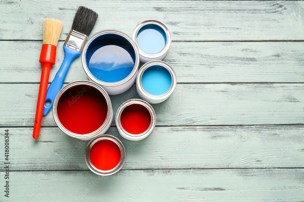 Cans of paints and brushes on color wooden background