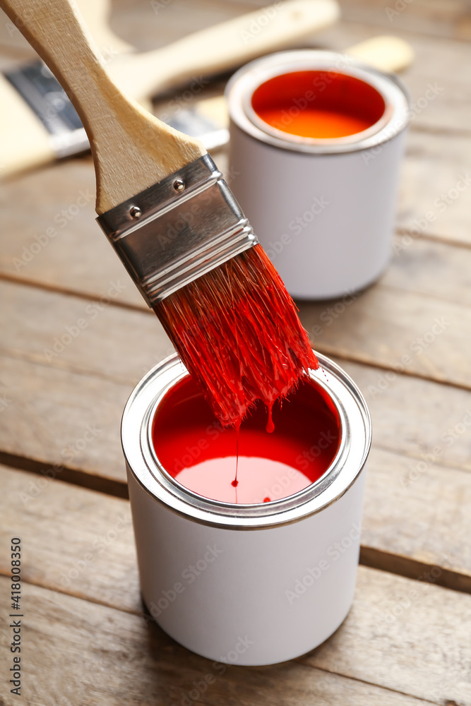 Brush and can of red paint on wooden background