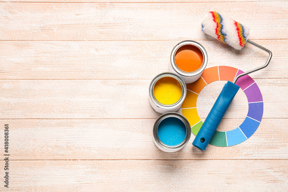 Cans of paints with palette samples and roller on color wooden background