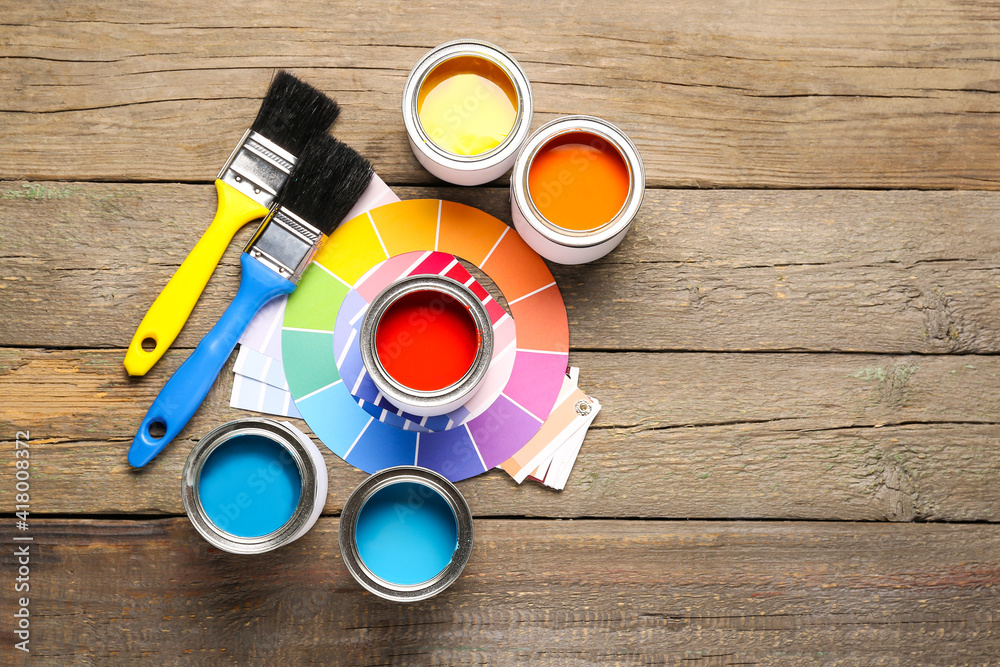 Cans of paints with palette samples and brushes on wooden background