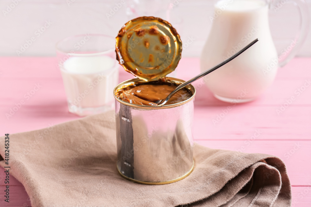 Tin can of boiled condensed milk on color wooden background