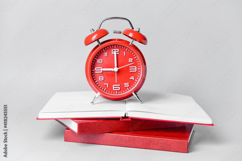 Alarm clock and blank books on light background