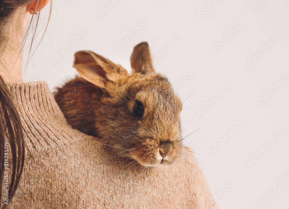 Young woman with cute rabbit on light background