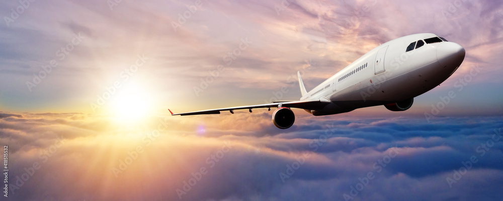 Passenger jetplane flying above clouds in sunset