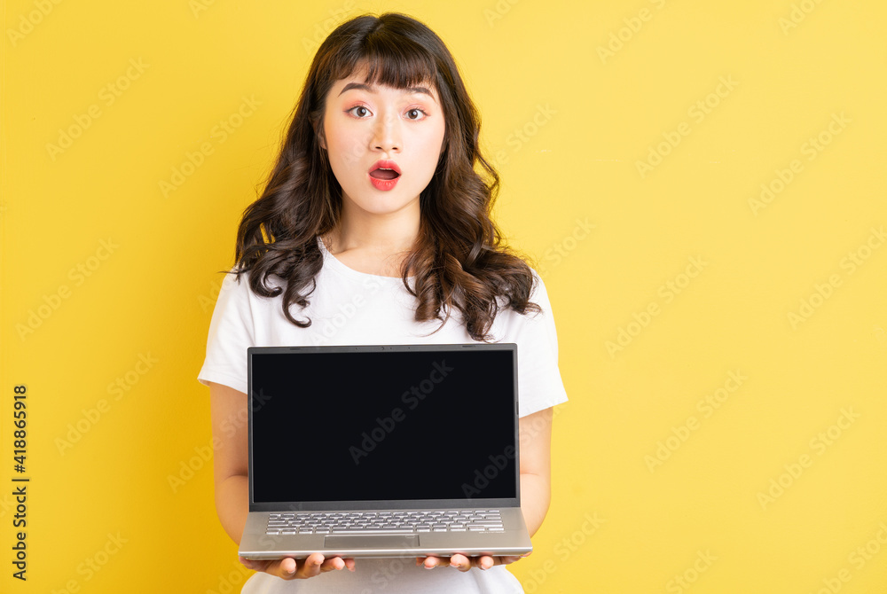 Young Asian woman holding laptop on yellow background