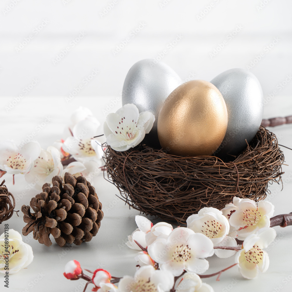 Close up of golden and silver Easter eggs in the nest with white plum flower.