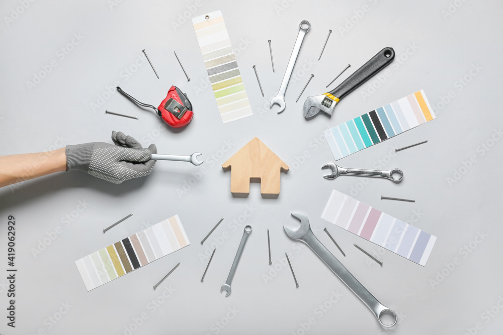 Female hand with figure of house and construction tools on light background