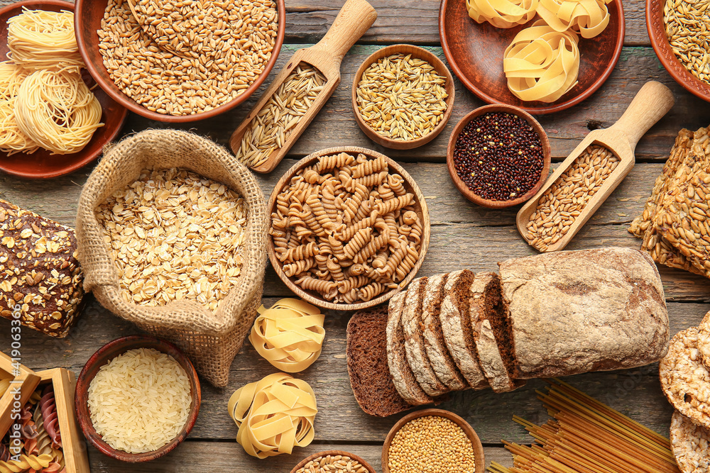 Different cereals, raw pasta and bread on wooden background