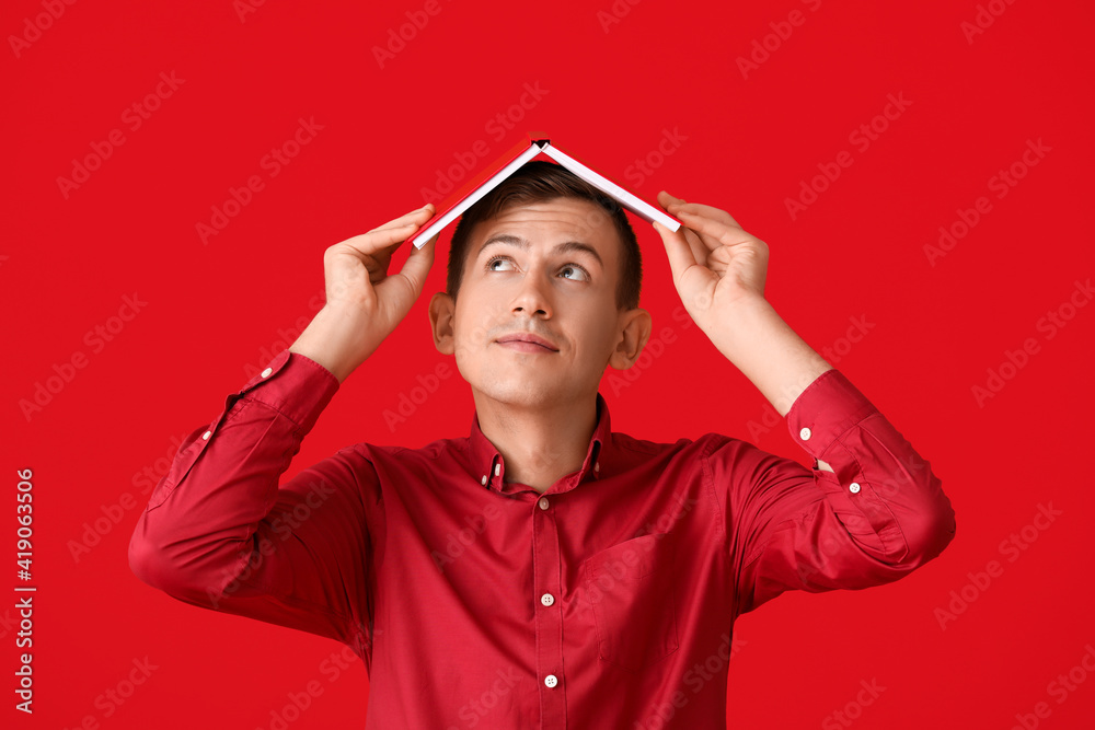 Young man with red book on color background