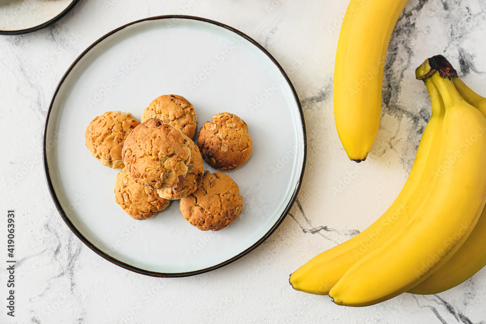 Plate with tasty cookies and bananas on light background