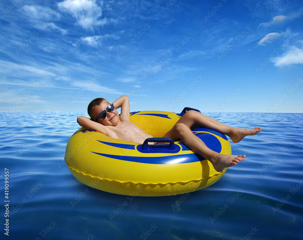 Little boy on inflatable ring in blue sea water surface .