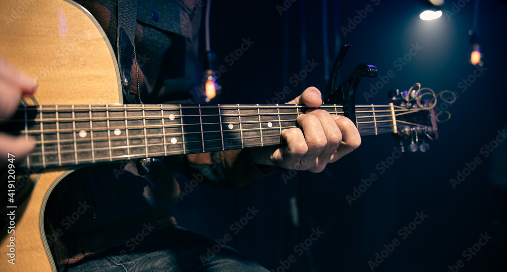 Close up a man plays an acoustic guitar in a dark room.