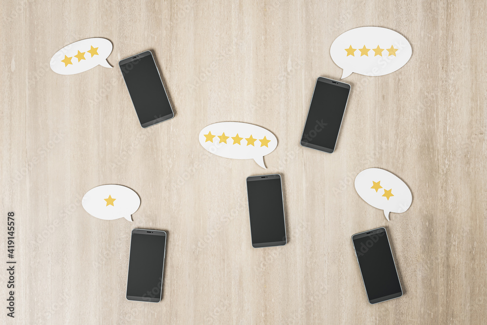 Rating feedback review concept with black smartphones on wooden surface and stars in speech bubbles