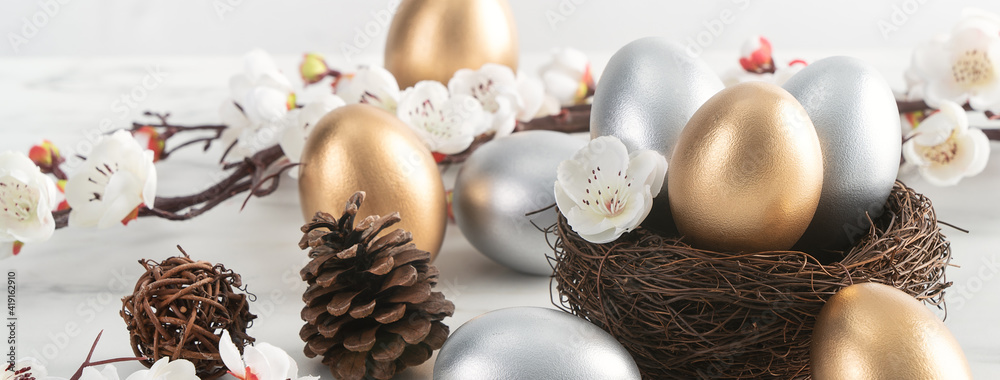 Close up of golden and silver Easter eggs in the nest with white plum flower.