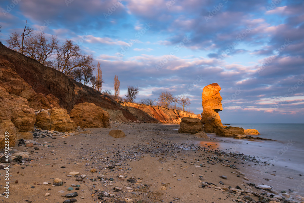 Sand beach with many small stones on the shore and big shell rock like statue from Easter Island on 