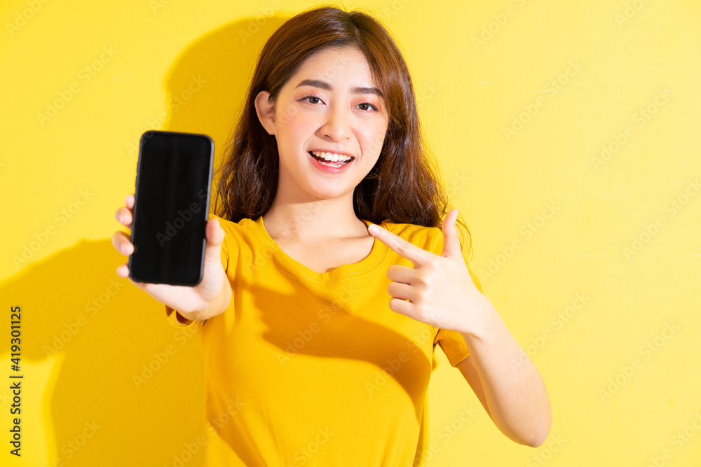 Young Asian girl uisng smartphone on yellow background