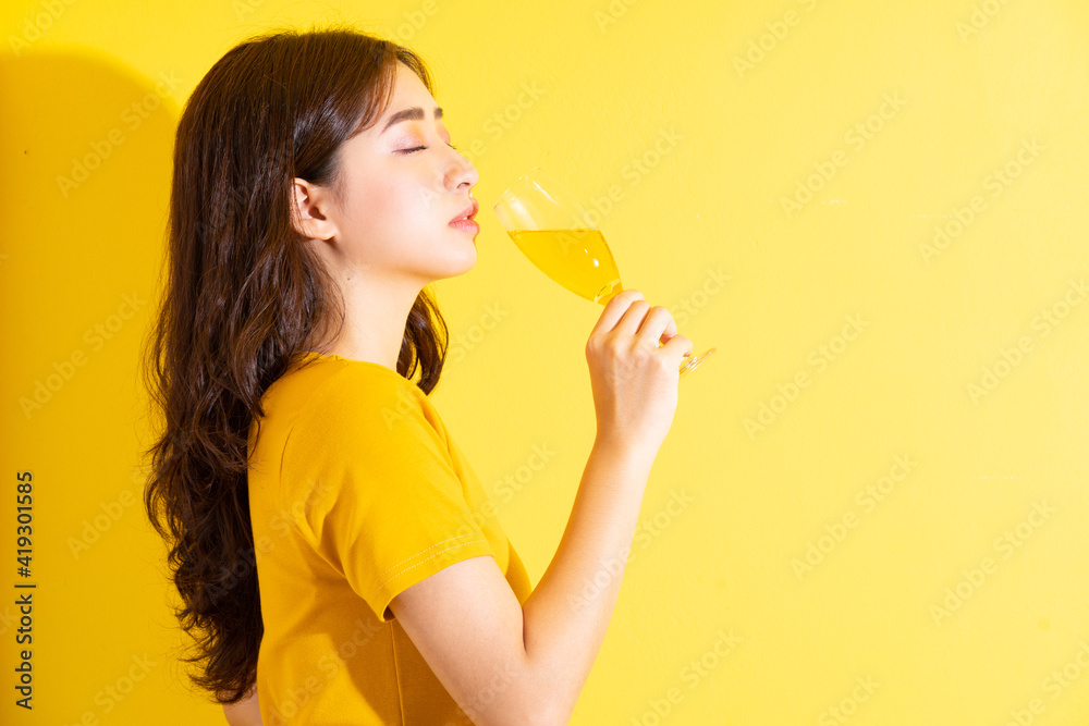 Young Asian woman drinking wine and posing on yellow background