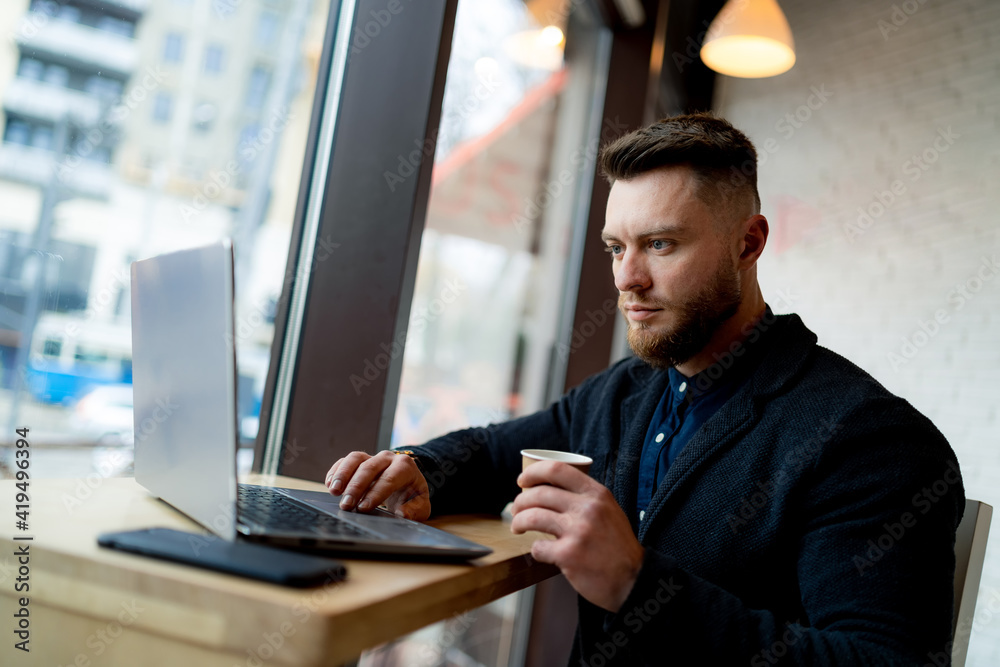 Stylish businessman doing work in beautiful cafe. Cup of cofee and phone is near him.