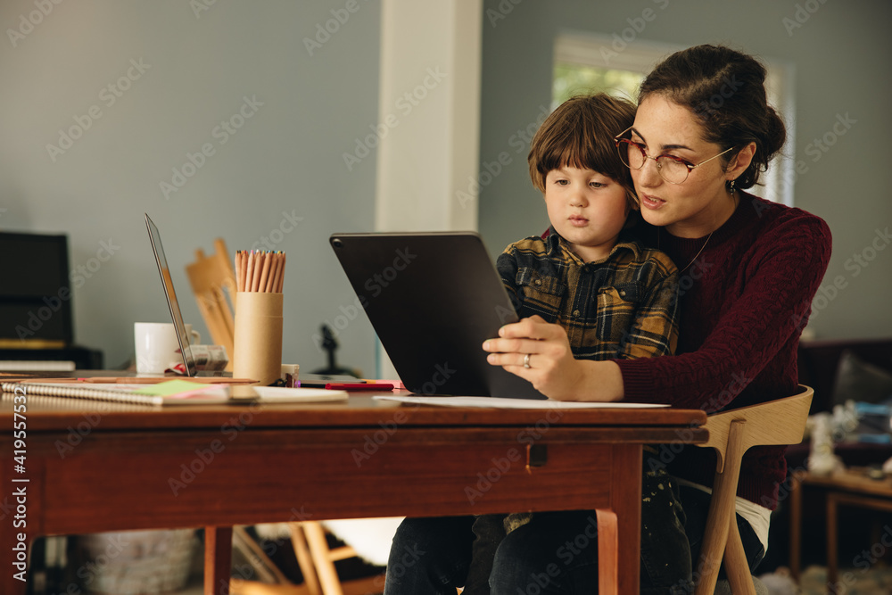 Mother using digital tablet with son homeschooling