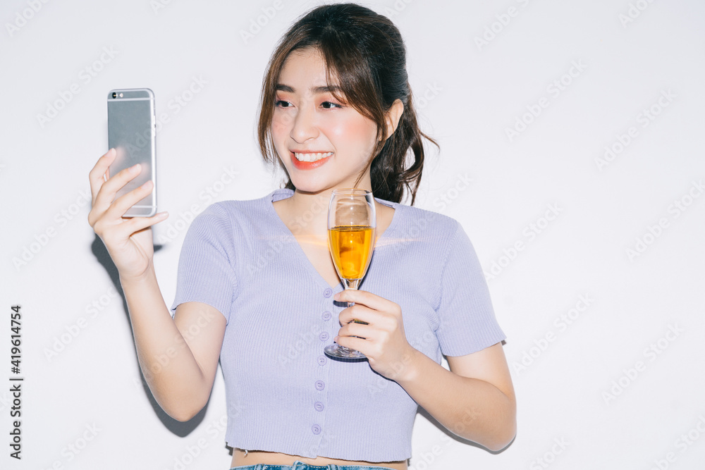 Young Asian woman drinking wine and using smartphone on white background