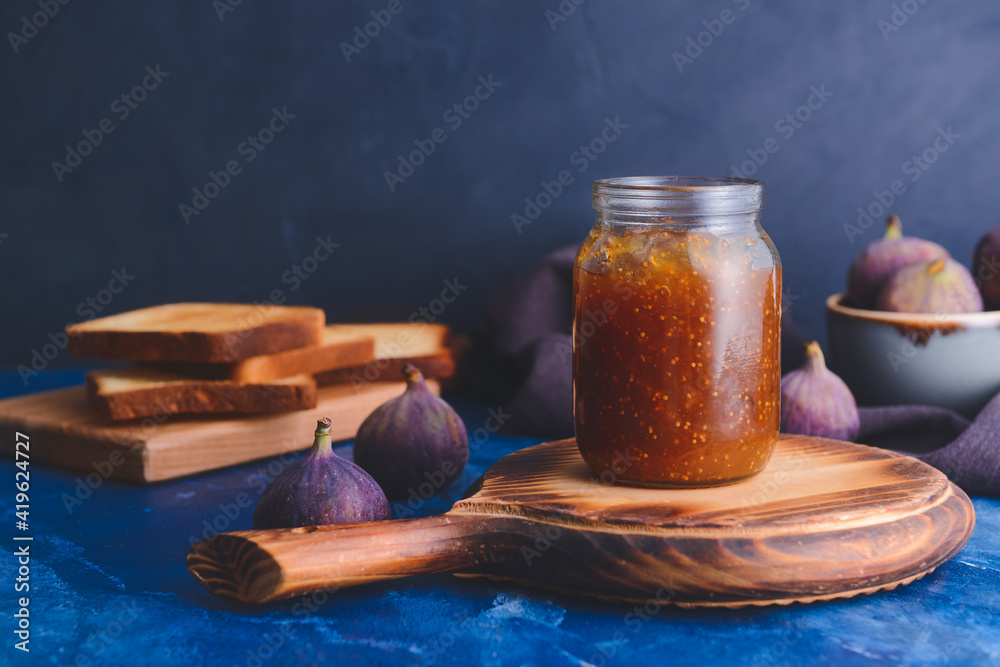 Glass jar with sweet fig jam on color background