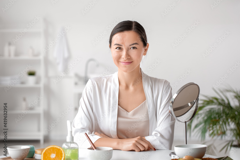 Beautiful young woman with facial mask in bathroom